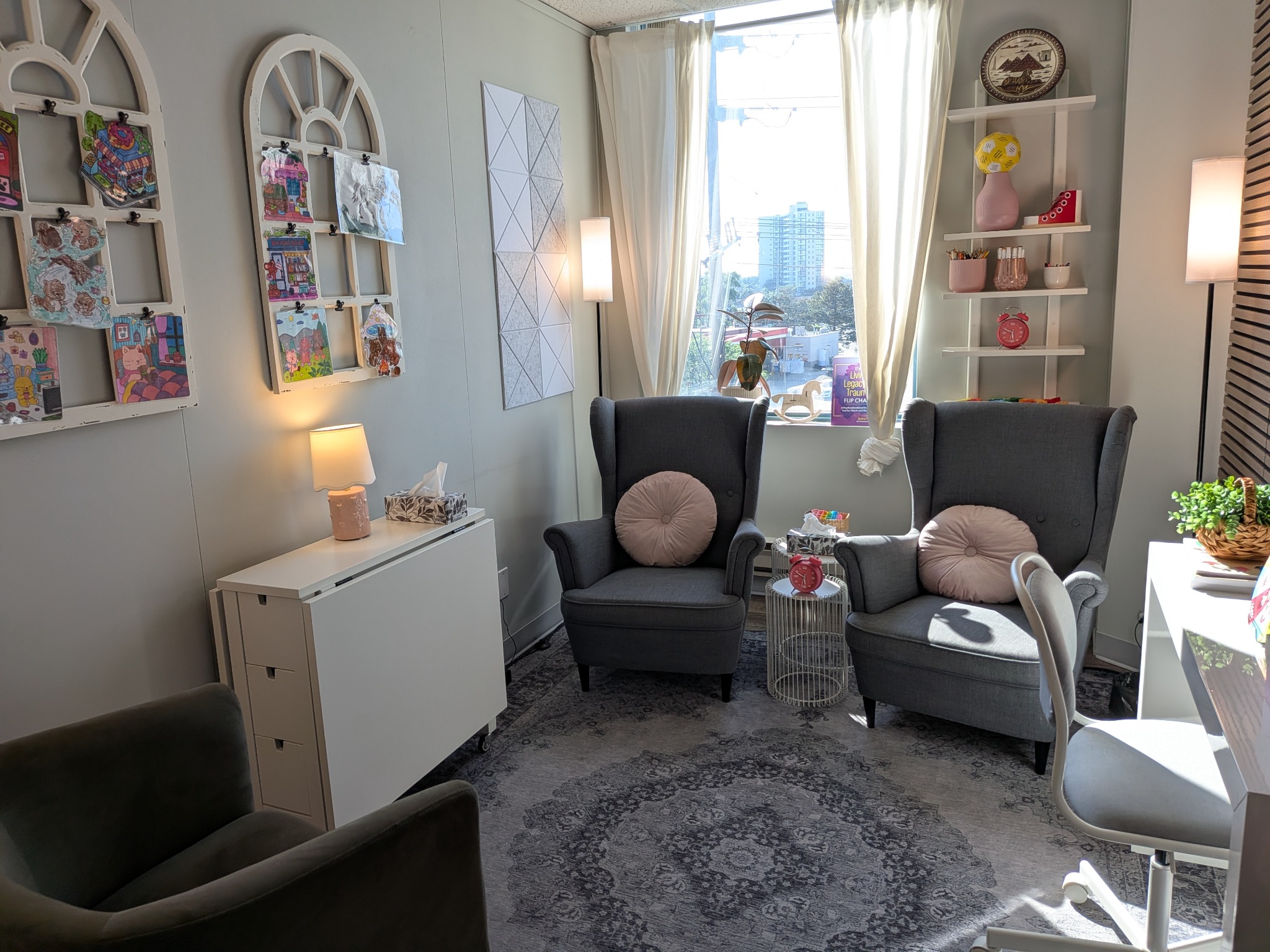 Bright child-friendly therapy room with two armchairs, artwork, toys, and a large window